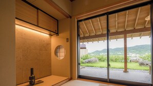 A traditional Japanese room with tatami flooring, a shoji screen door, and a view of a garden and mountains.