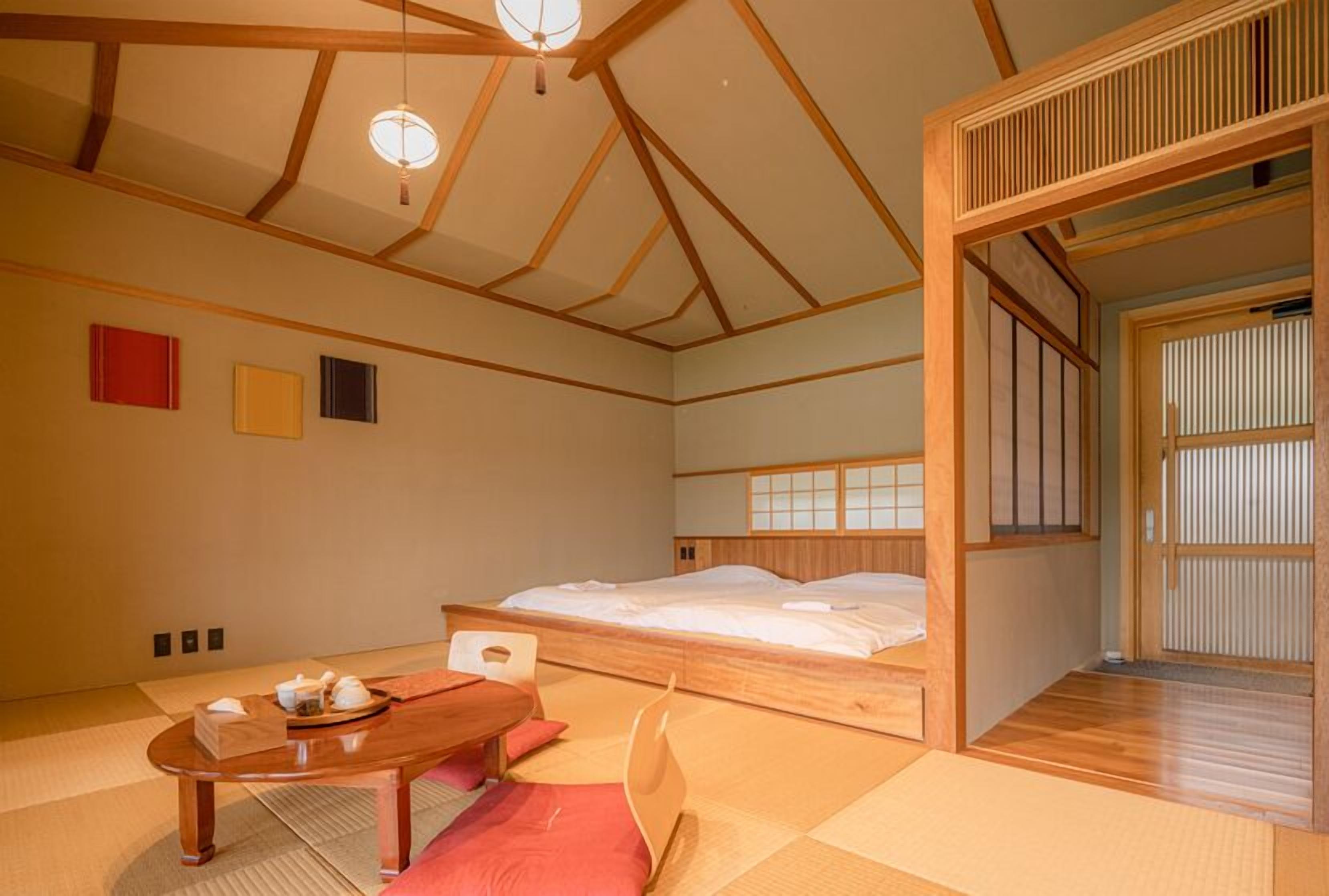 A traditional Japanese-style room with tatami flooring, a low wooden bed, a wooden table with a tea set, and shoji screens.