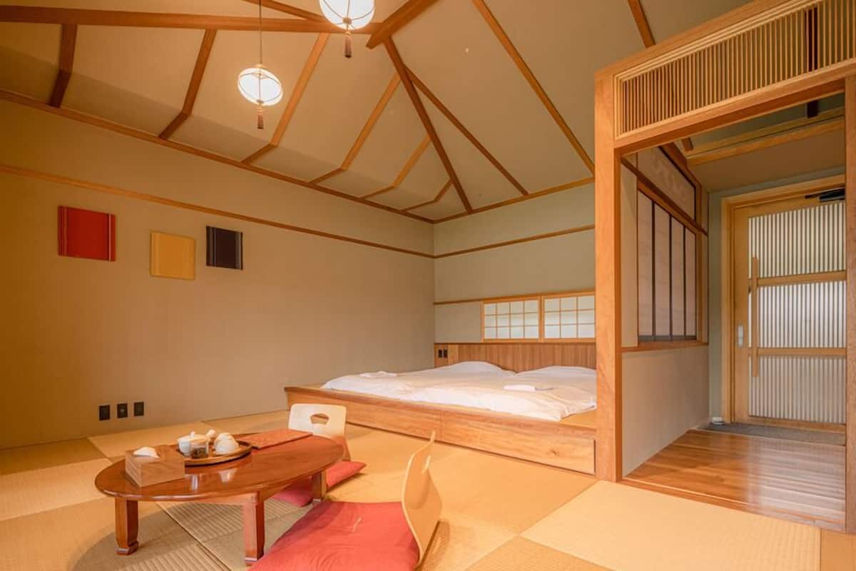Une pièce de style japonais traditionnel, avec un sol recouvert de tatamis, un lit bas en bois, une table en bois avec un service à thé et des paravents shoji.