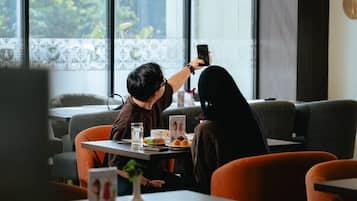 Una persona tomando una foto con un teléfono inteligente, sentada a una mesa con una computadora portátil y un vaso de agua.