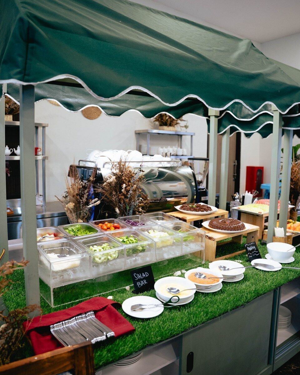 Montaje de bufé con diferentes recipientes de comida, barra de ensaladas y una máquina de café.