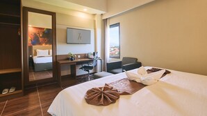 Una habitación de hotel con cama, escritorio, silla y un ventanal amplio.