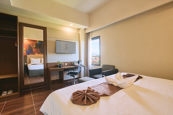 A hotel room with a bed, desk, chair, and a large window. - Horison Ultima Sayaga Cibinong (Cibinong)