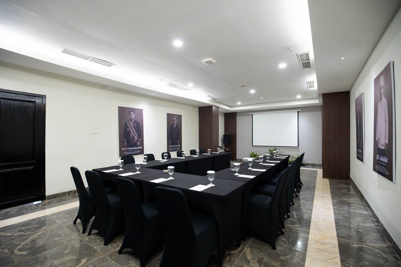 Un salón de conferencias con una larga mesa, sillas, una pantalla de proyector y carteles en las paredes.
