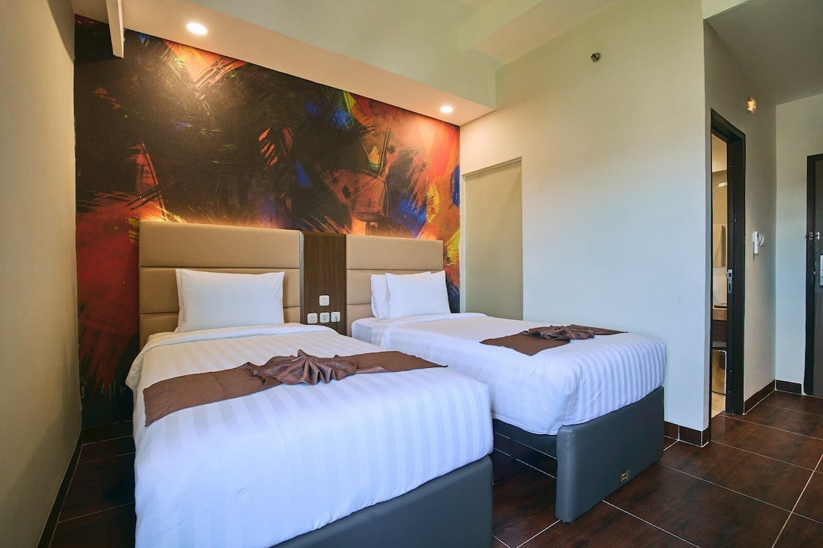 A hotel room with two beds, a large abstract painting on the wall, and a modern design.