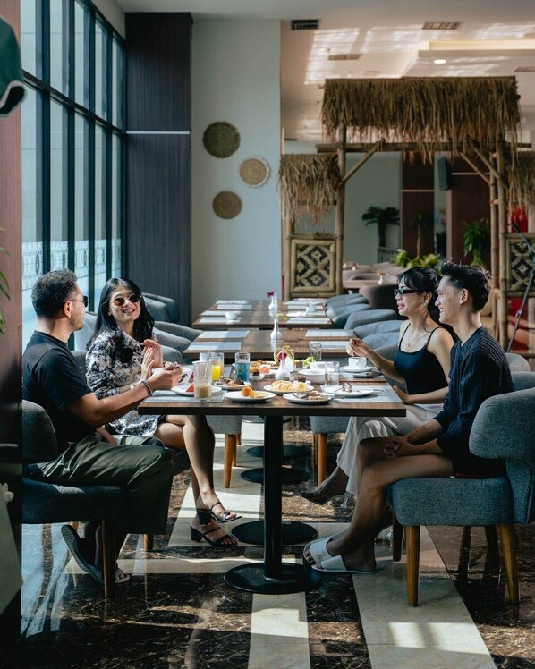 Un groupe de personnes est réuni dans un restaurant à l’intérieur moderne, avec notamment un mur décoré de motifs et un plafond en chaume.