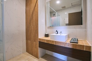 A modern bathroom with a marble floor, a wooden accent wall, a white sink, and a large mirror. - Horison Ultima Sayaga Cibinong (Cibinong)