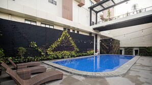 A swimming pool with lounge chairs and a black wall with plants. - Horison Ultima Sayaga Cibinong (Cibinong)