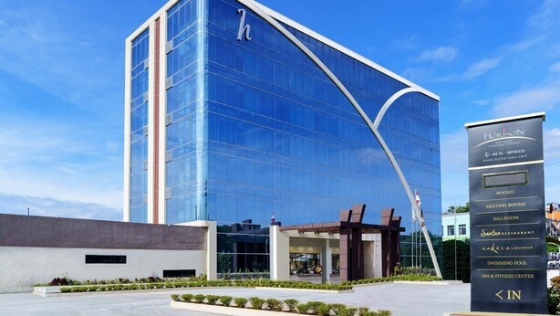 Un hotel moderno con fachada de vidrio, un llamativo logotipo en forma de 'h' y un letrero que anuncia servicios como salas de reuniones, un salón de baile y un spa.