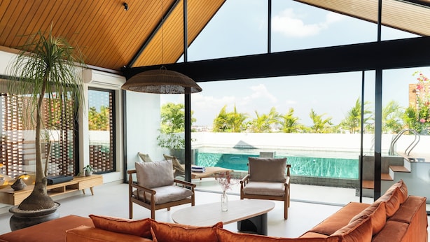 A modern living room with a large window, a pool view, and a wooden ceiling. - Makia Penthouse by Alfred in Bali (Canggu)