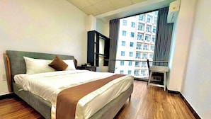 A hotel room with a large bed, a wooden floor, a desk, and a view of a building through the window. - Bros Citihouse (Ho Chi Minh City)