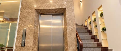 Un ascenseur moderne aux finitions métalliques, un escalier avec des rampes en bois et une pancarte sur laquelle on peut lire : « Partagez l’amour ».
