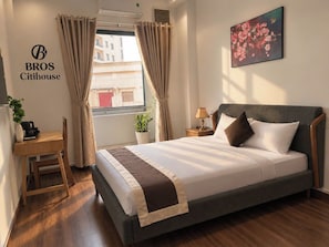 Una habitación de hotel con cama, mesita de noche, lámpara y ventana con cortinas.