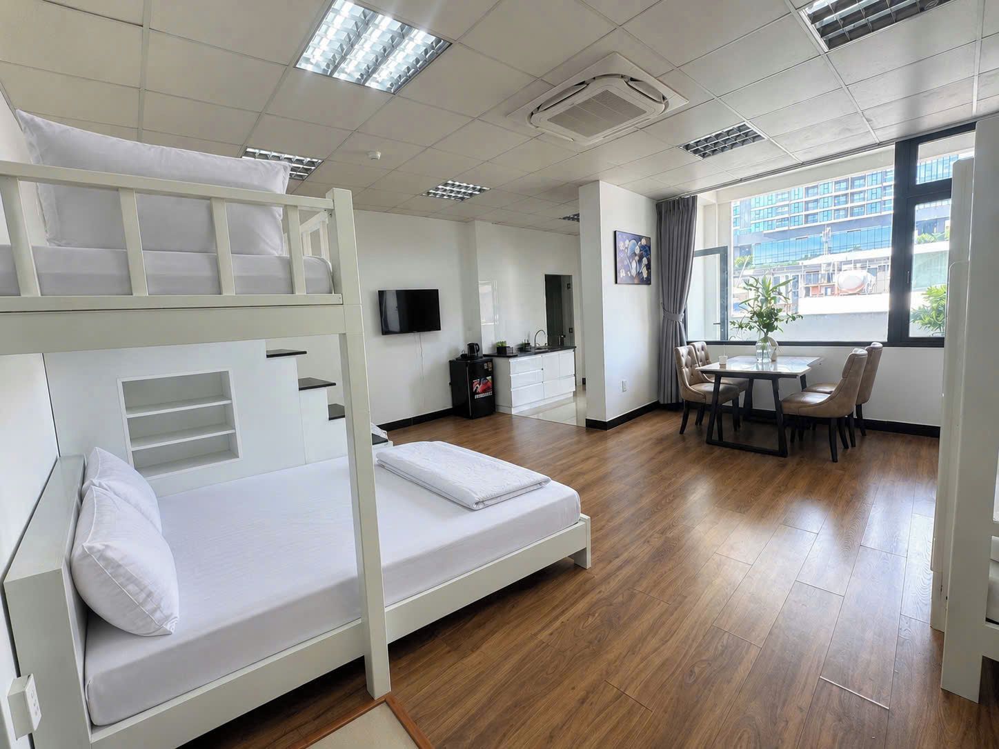 A bunk bed room with a desk and chair, a television, and a window with a view of buildings.