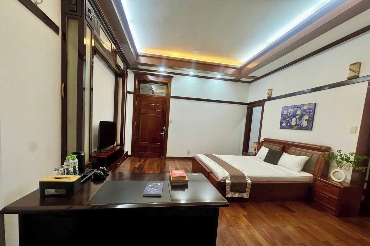 Een hotelkamer met een houten bureau, een bed, een televisie en een schilderij aan de muur.