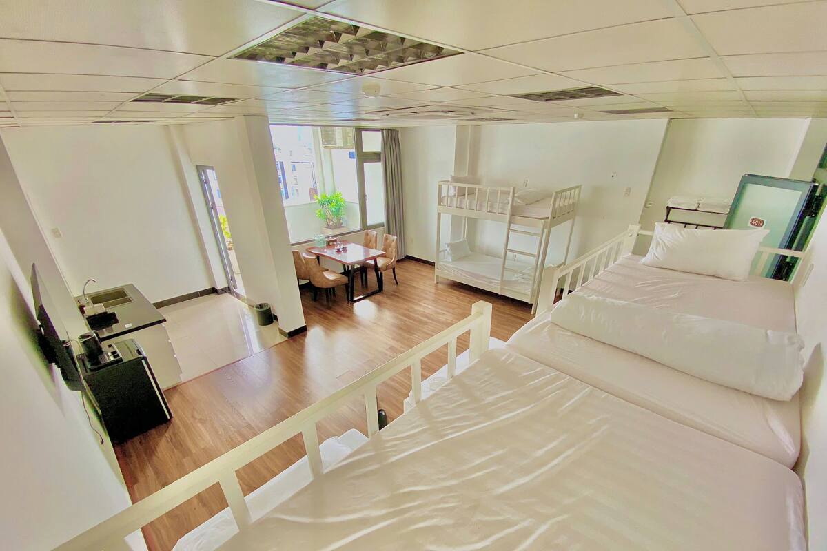Een hotelkamer met stapelbedden, een bureau met stoel, een klein tafeltje en een potplant.