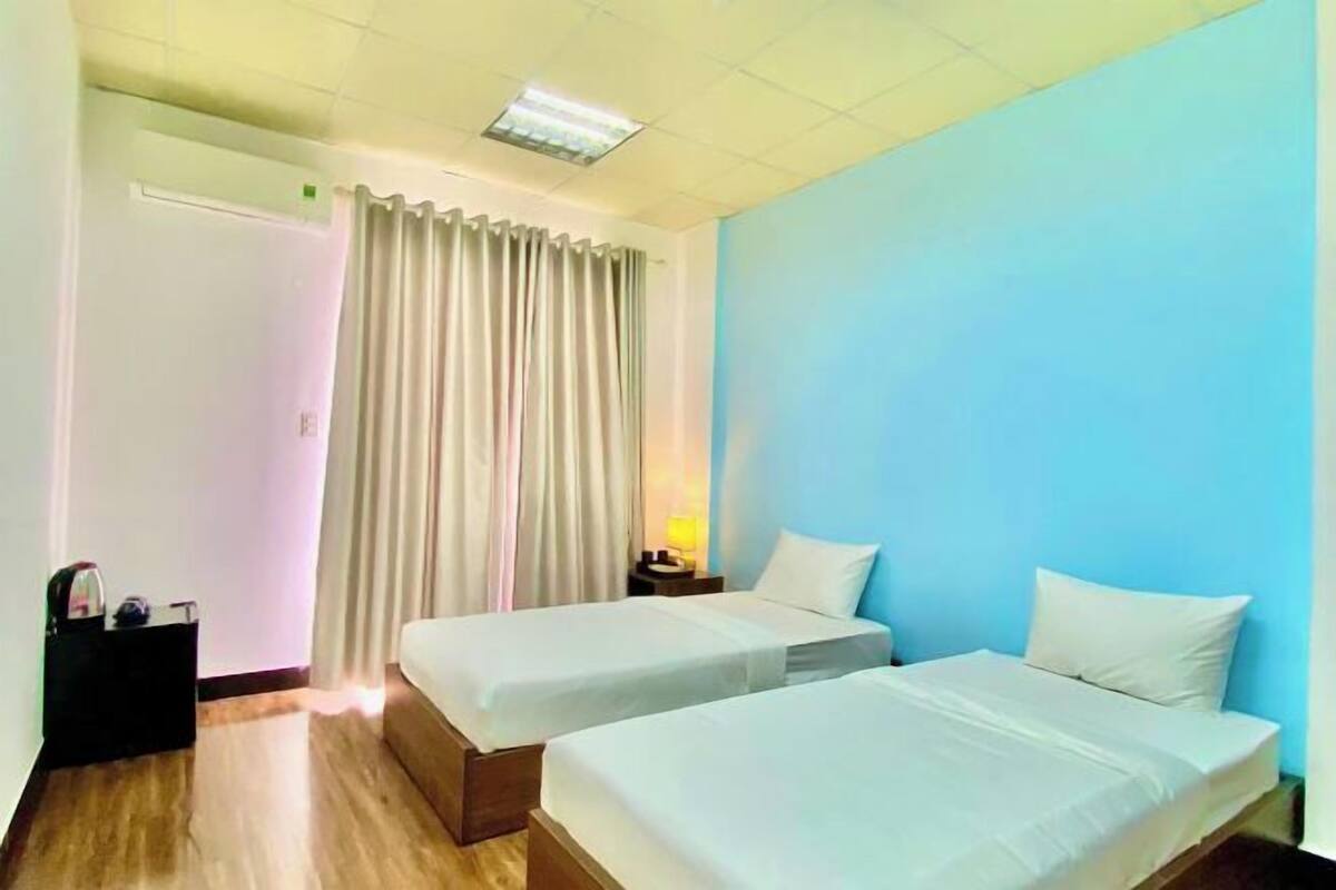 Hotelkamer met twee eenpersoonsbedden, een nachtkastje met een lamp, een houten vloer, een deur en een raam met gordijnen.