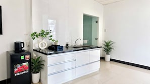 Une cuisine moderne avec un réfrigérateur noir, des armoires blanches, un plan de travail noir et une porte en verre donnant sur une salle de bain.