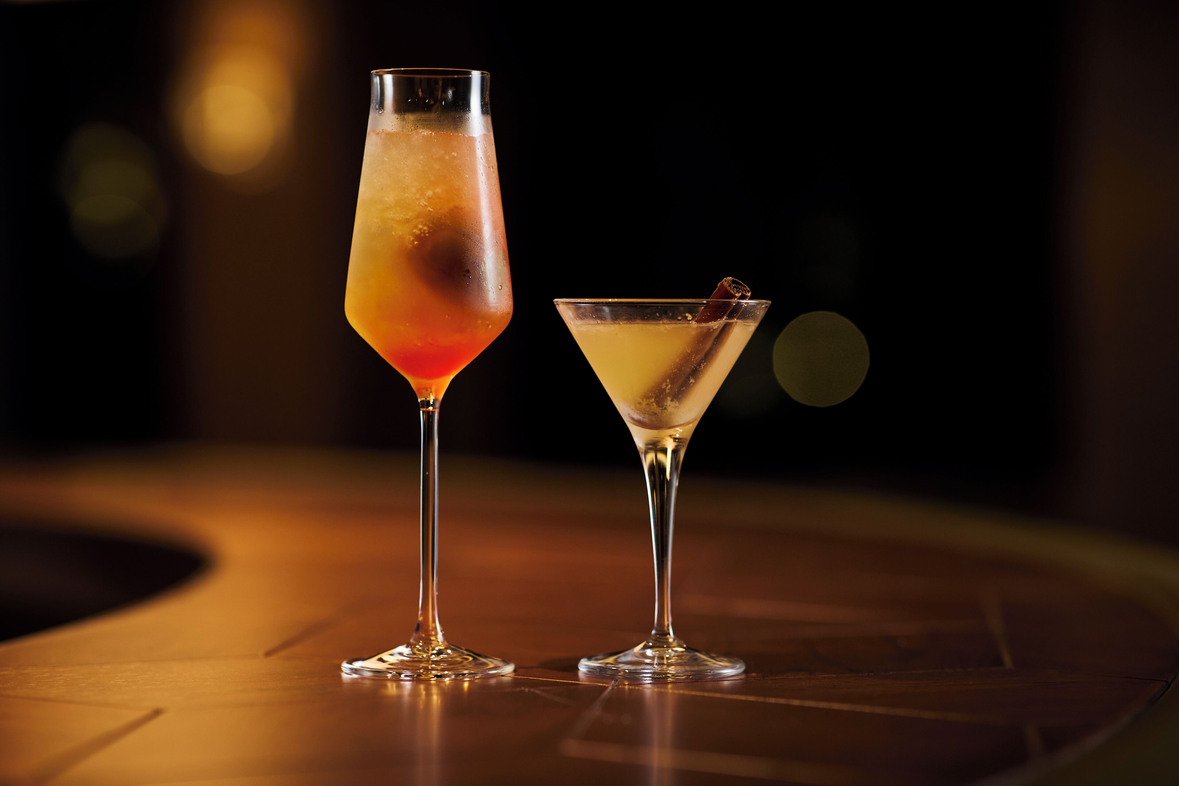 Two cocktails on a wooden table with a blurred background.