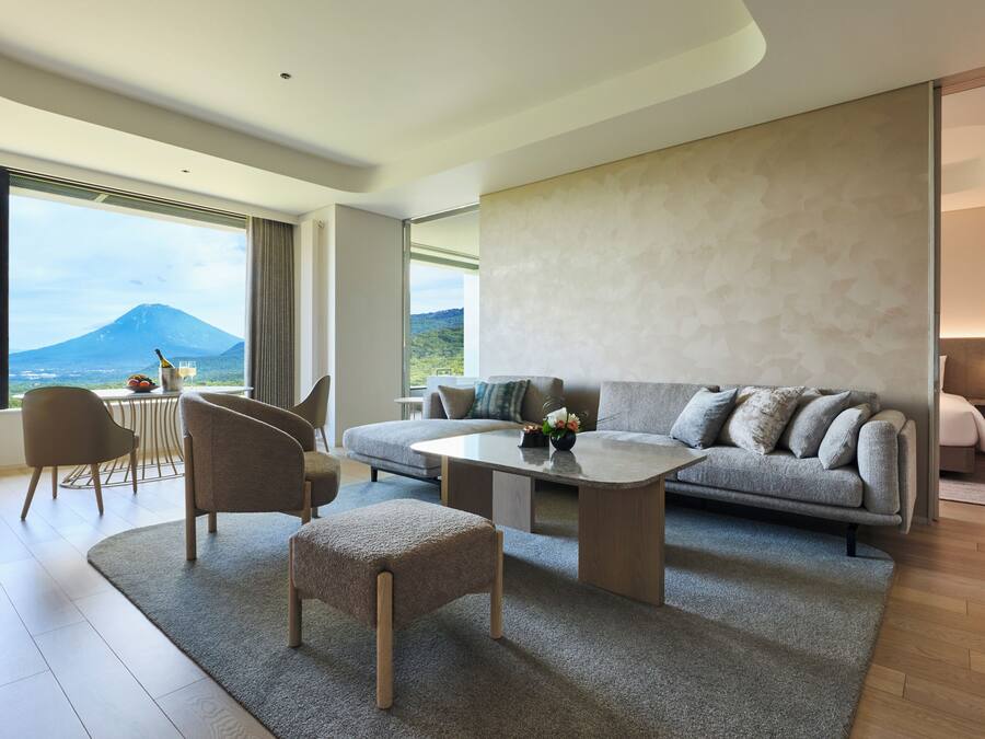A modern living room with a sofa, coffee table, and ottoman, large windows with a mountain view, and a minimalist design.