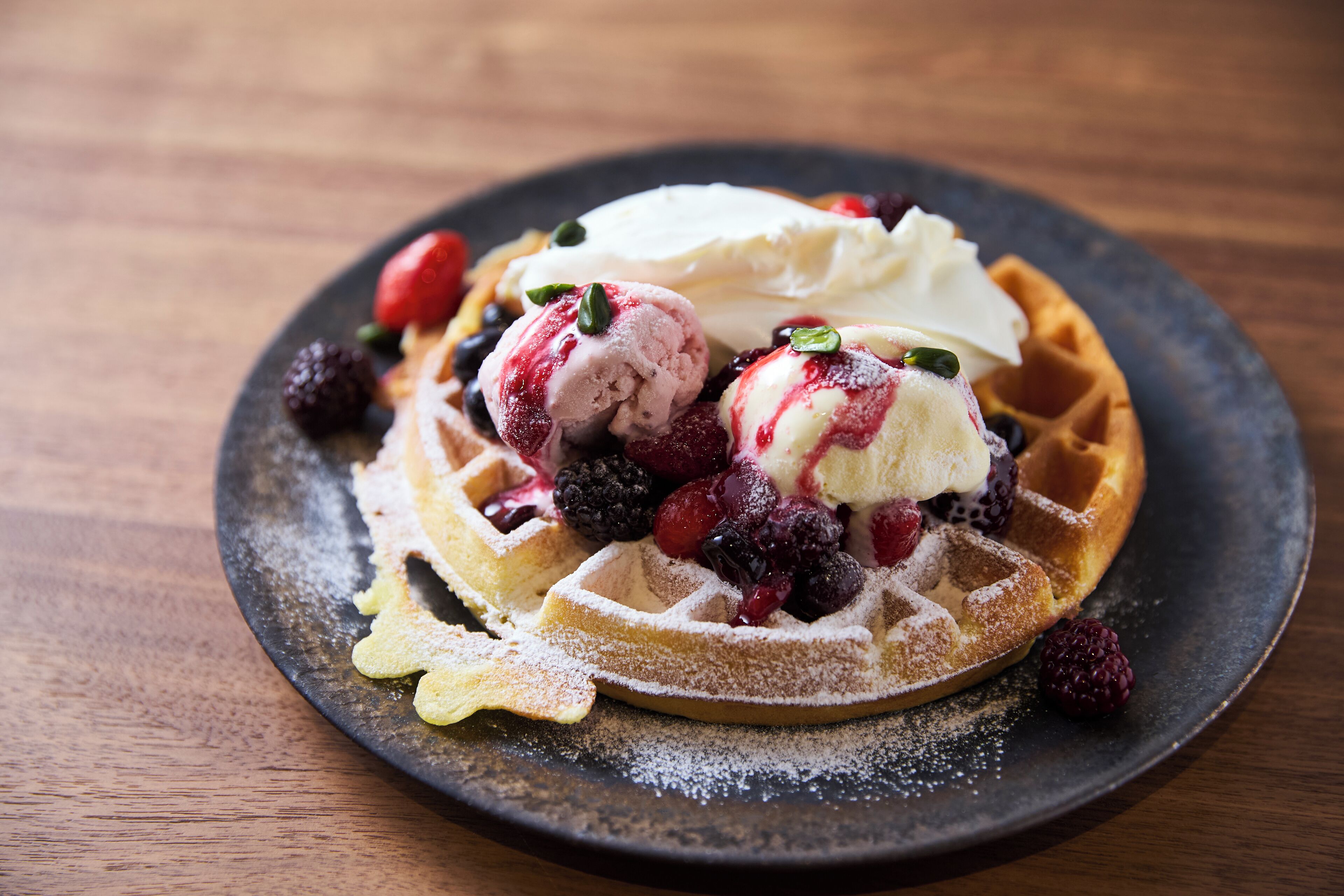 Waffle com sorvete e frutas vermelhas num prato.