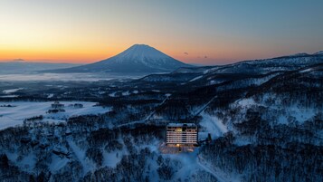 Un hotel de varios pisos, rodeado de bosques nevados y una montaña al fondo.