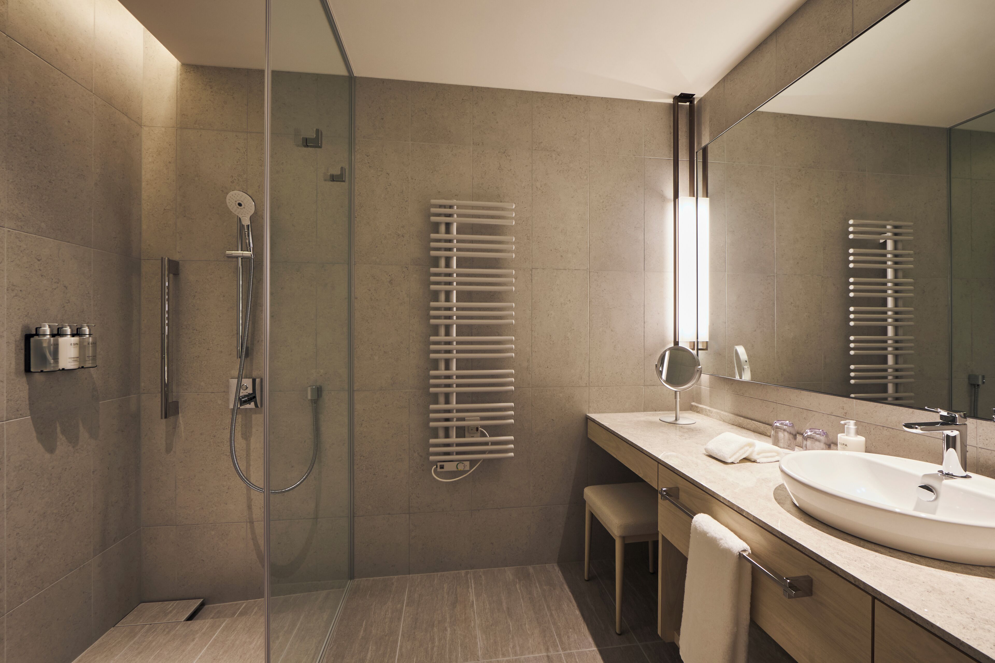 Een moderne badkamer met een glazen douchecabine, een grote spiegel, een beige wastafel en een handdoekrek.