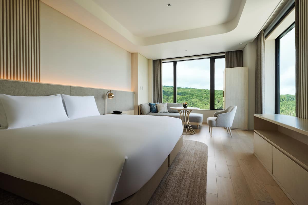 A modern hotel room with a large bed, a seating area with a table, and a view of the outdoors.