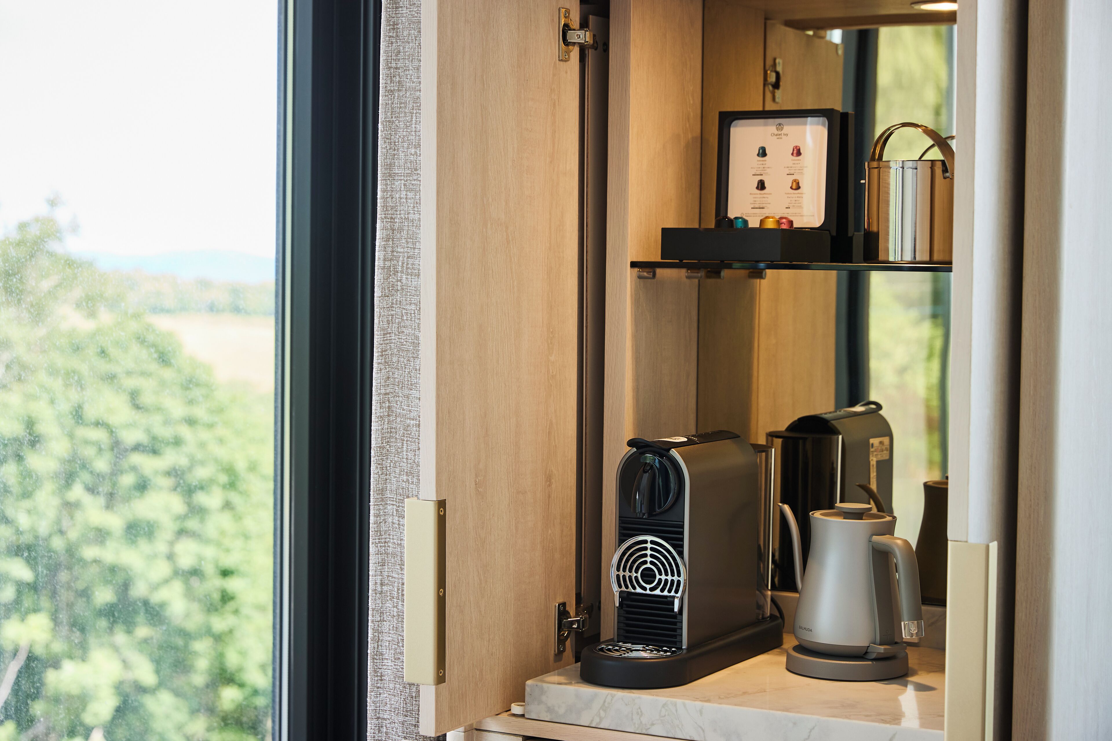 Een kleine keuken met een koffieapparaat, een waterkoker en een klein plankje met een koffiezetapparaat en een verpakking.