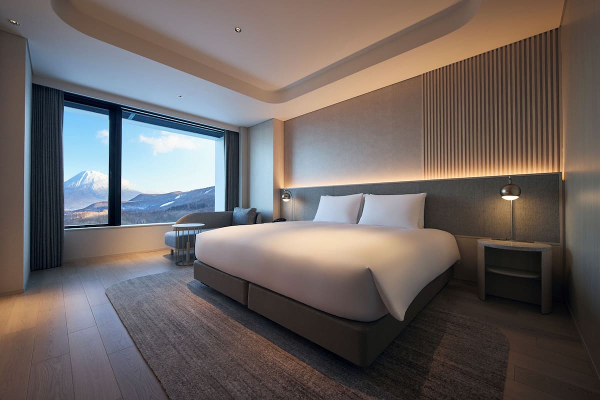 A modern hotel room with a large bed, a view of a mountain, and a minimalist design.