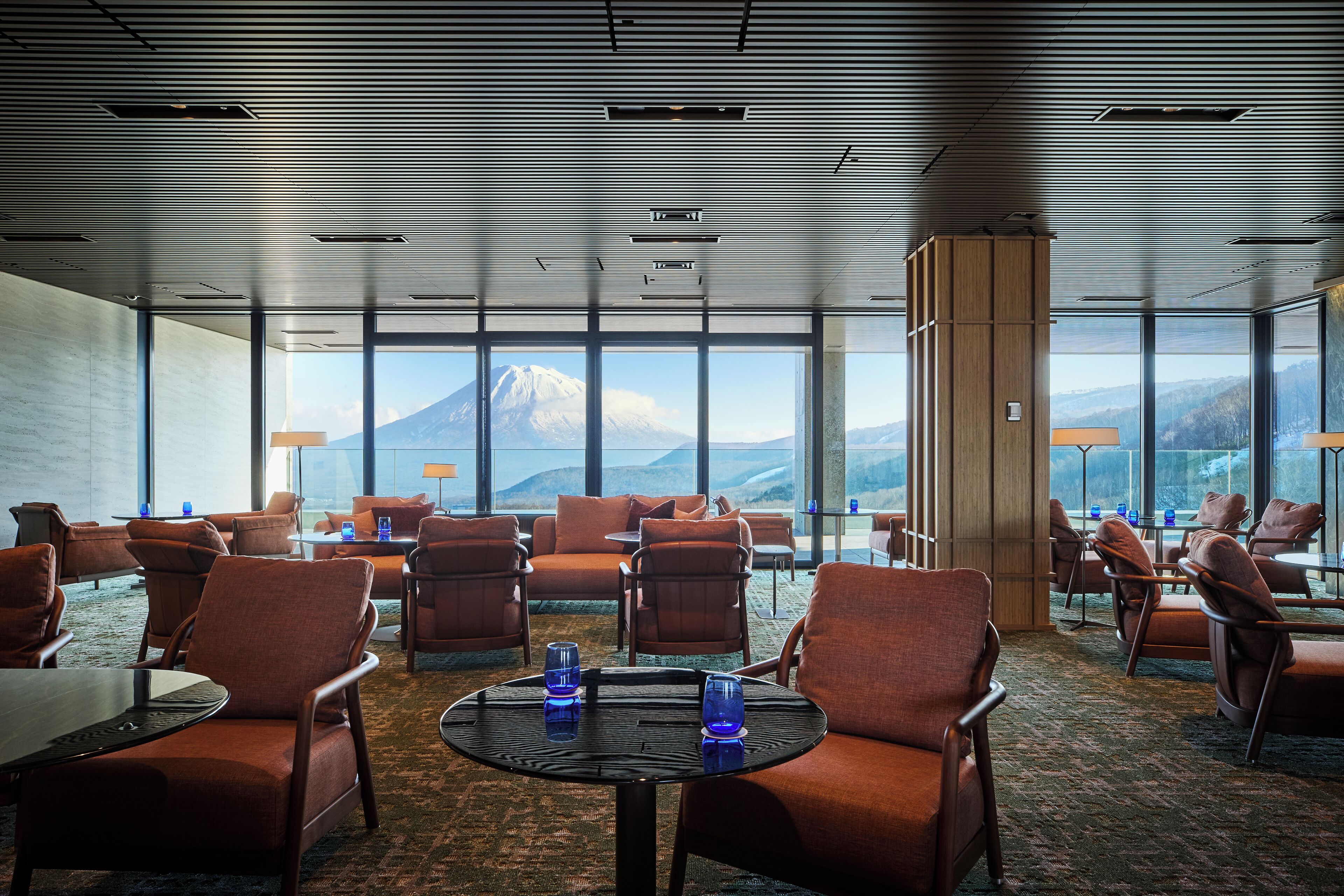 Un hall d’hôtel avec vue sur une montagne, aménagé avec des fauteuils et des tables en cuir, et orné d’une grande colonne.