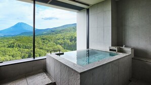 Un baño moderno con una bañera grande y vistas a una montaña boscosa.