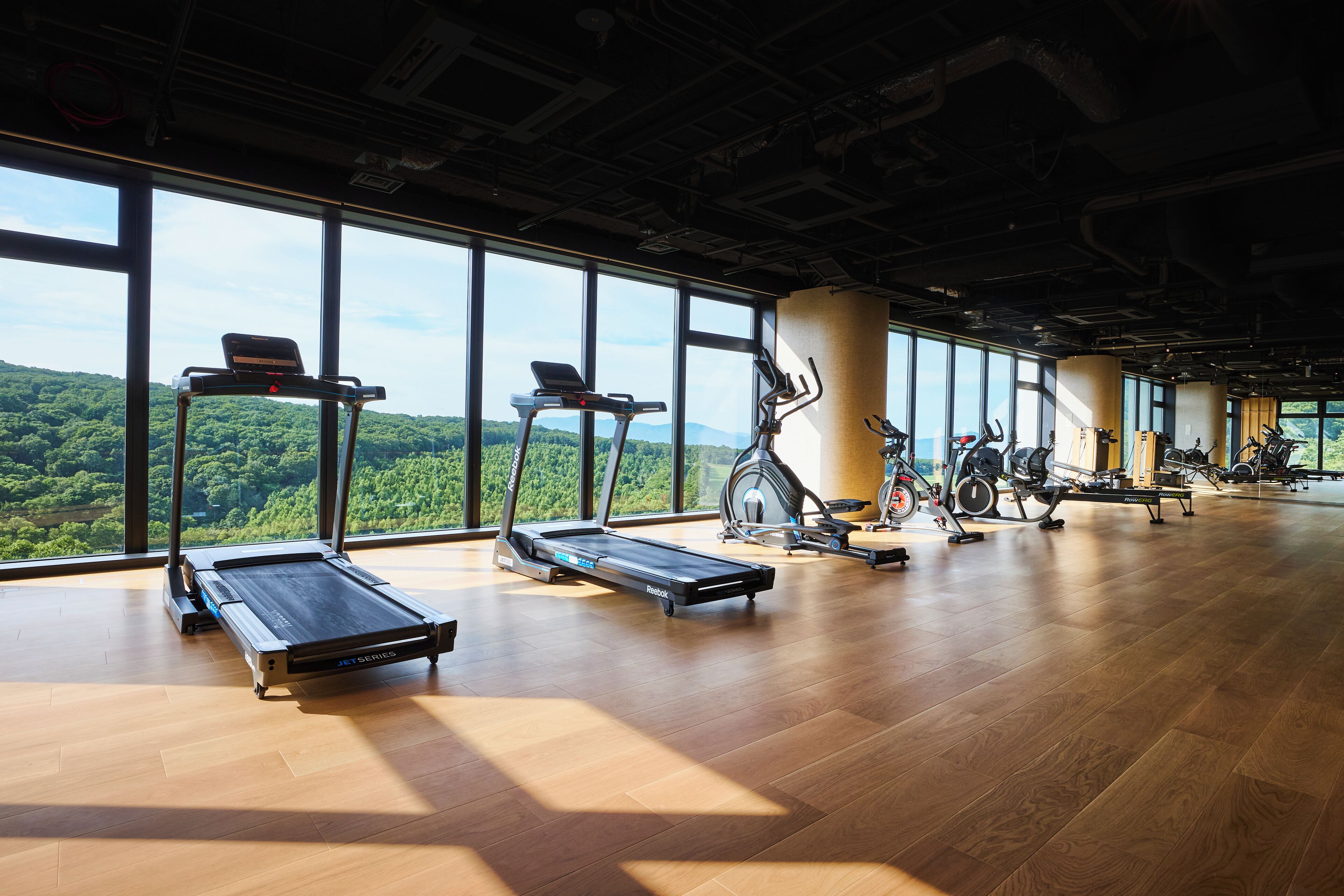 Una palestra con diverse attrezzature per esercizi, ampie finestre e un pavimento in legno.