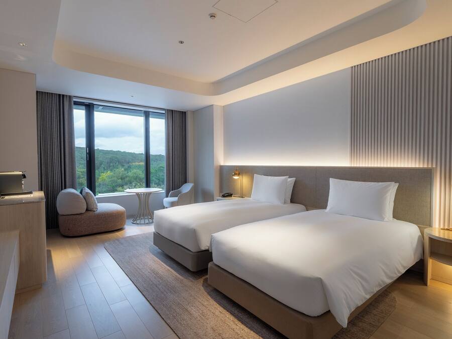 Una habitación de hotel moderna con dos camas, un escritorio, una silla y vistas al exterior.