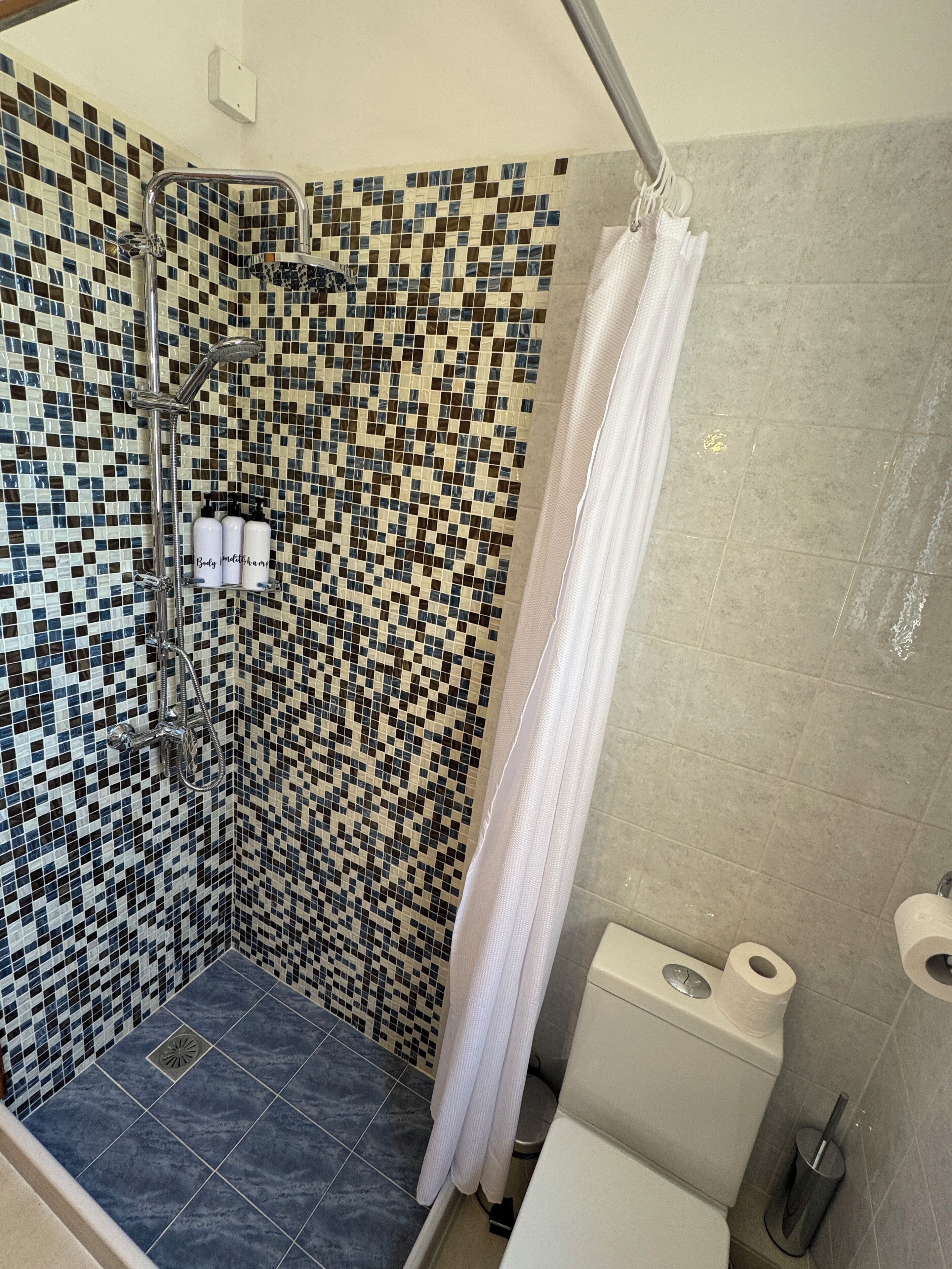 Ein Duschbereich mit einer mosaikverzierten Wand, einer Duschbrause und einem Duschvorhang.