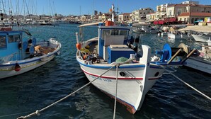 Un puerto deportivo con varias embarcaciones amarradas, cielo despejado y edificios al fondo.