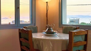 Un área de comedor con una mesa dispuesta para dos, una lámpara de pie y amplias ventanas que ofrecen vista al mar y montañas distantes.