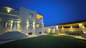 Una casa moderna de dos pisos con un exterior bien iluminado, un área de estar cubierta al aire libre y una escalera visible que conduce a la entrada.
