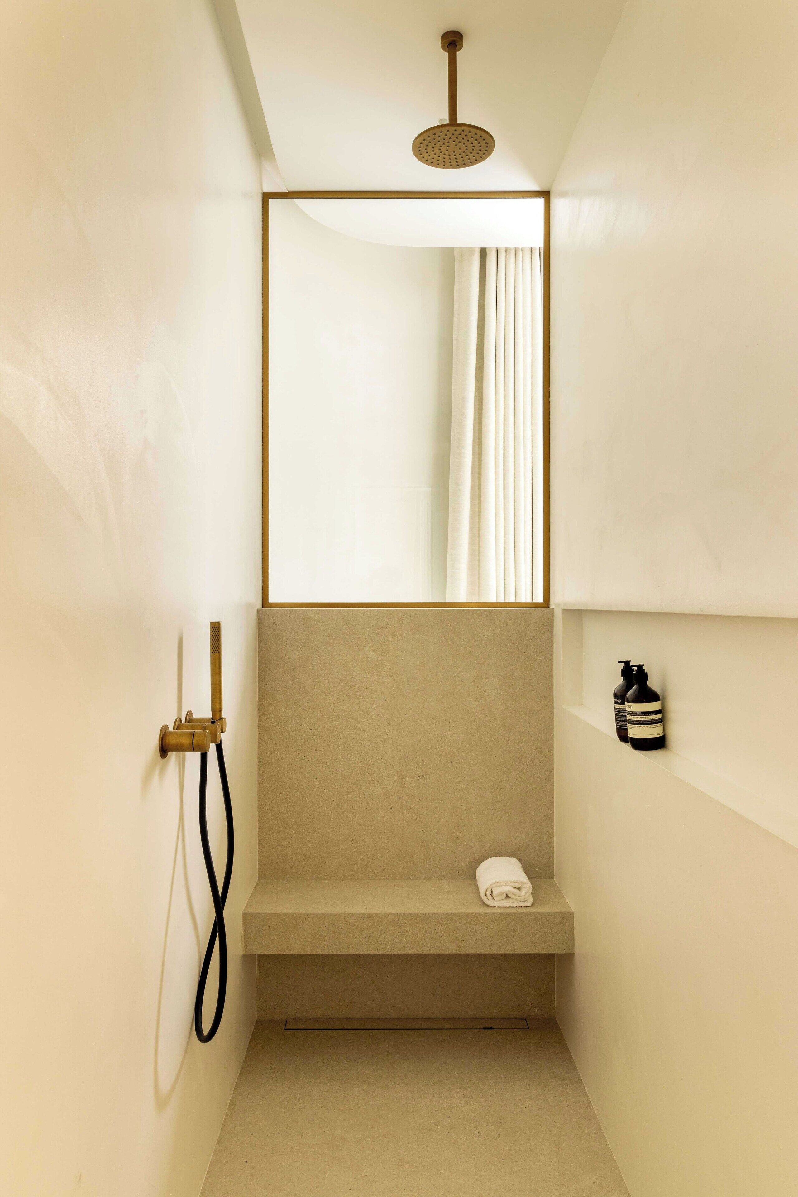 Een moderne badkamer met een douche, een zitbankje en een spiegel.