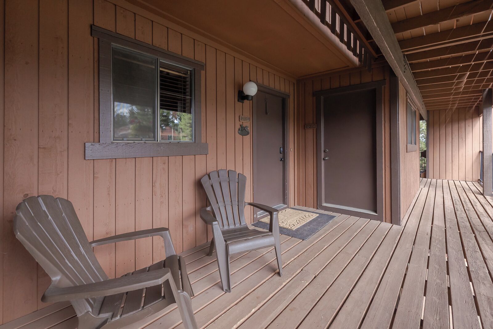 Eine hölzerne Veranda mit zwei Adirondack-Stühlen, einer Tür und einem Fenster mit Jalousien.