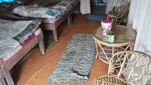 A room with two beds, a woven rug, a wicker chair, and a table with a can of drink. - Rudraksh Valley Camp (Pokhri)