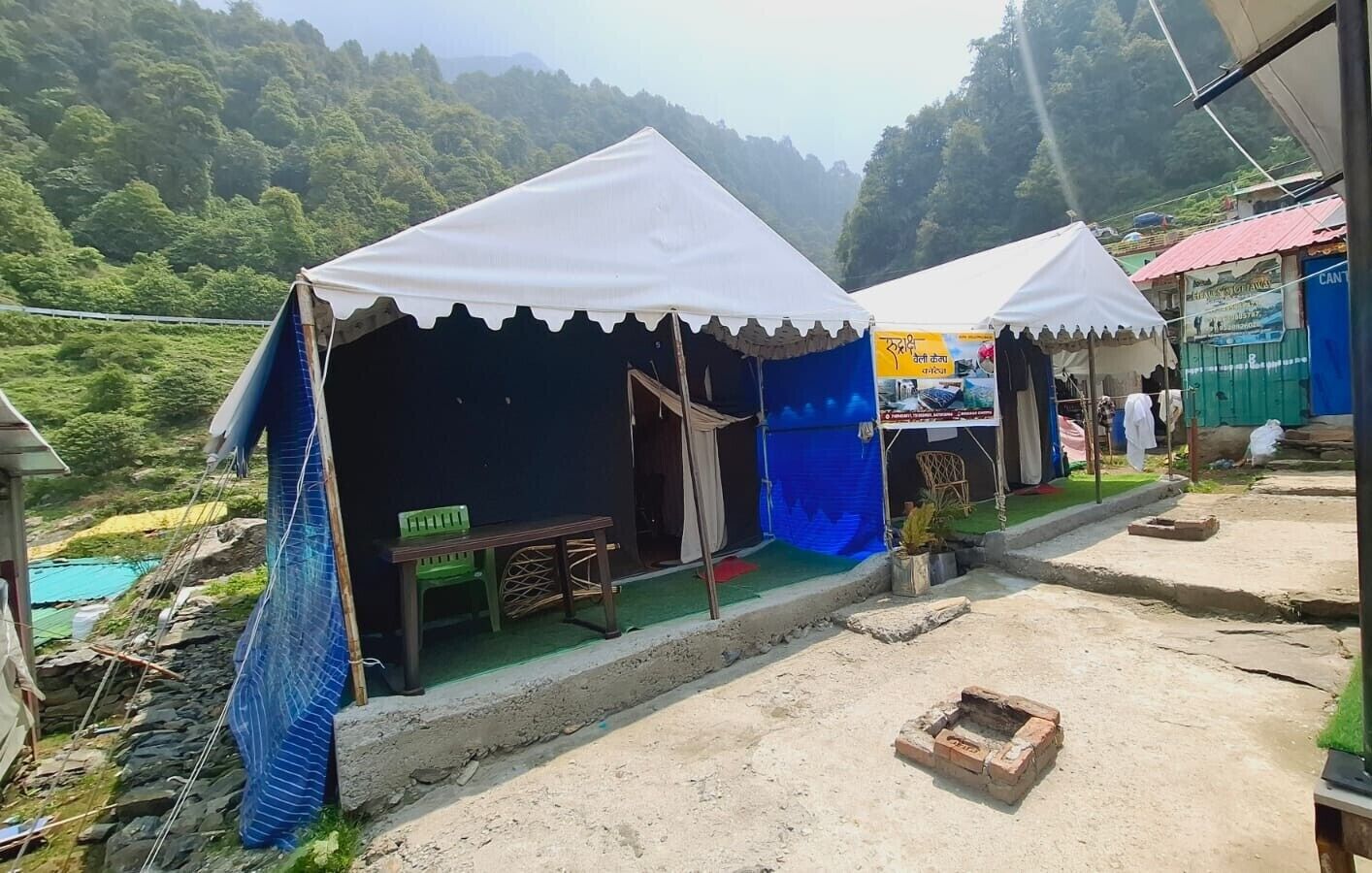 Two white tents with a table and chairs in front, set against a mountainous backdrop.