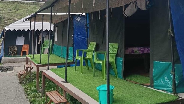 A camping site with tents, green plastic chairs, a picnic table, and a grassy area. - Rudraksh Valley Camp (Pokhri)