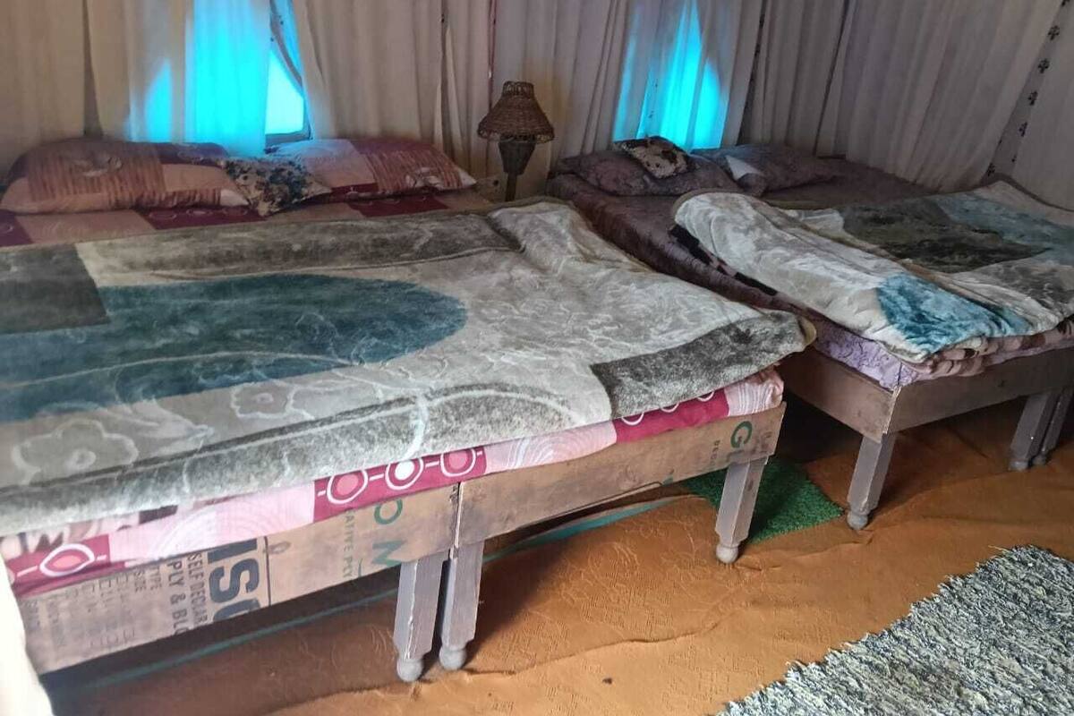 Ein Zimmer mit zwei Betten, jedes mit gemusterten Bettbezügen und einer Lampe dazwischen.