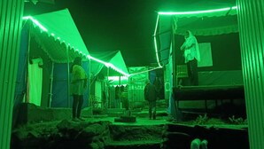 A courtyard with tents and people, surrounded by buildings with green lighting. - Rudraksh Valley Camp (Pokhri)
