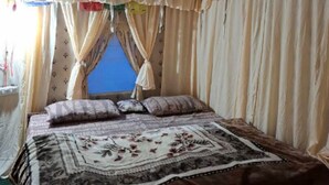 A bedroom with a bed, curtains, and a window. - Rudraksh Valley Camp (Pokhri)
