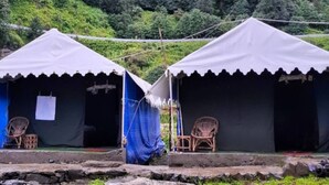 Two white tents with blue curtains, each with a wicker chair and a small table. - Rudraksh Valley Camp (Pokhri)