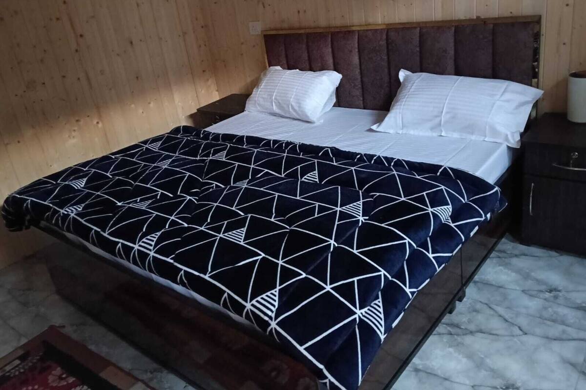 Ein Bett mit einem geometrisch gemusterten Überwurf, einem Holzkopfstück und weißen Kissen.