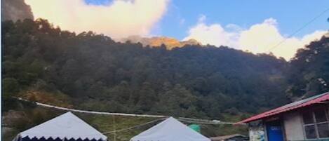 A mountainous landscape with a clear sky. There are tents and a small building with a red roof.