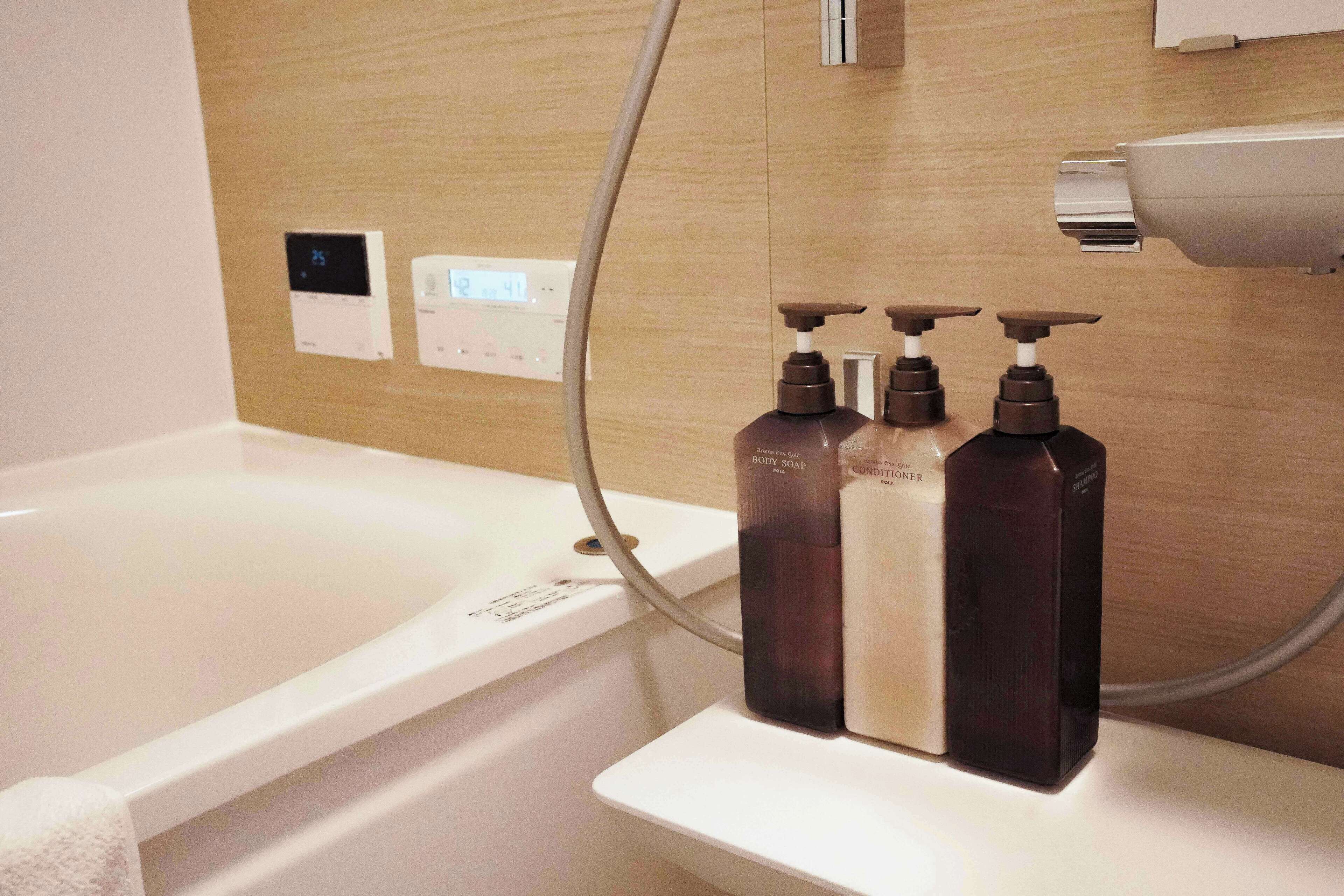 A bathroom with a bathtub, a shower head, and three bottles of body soap on a shelf.